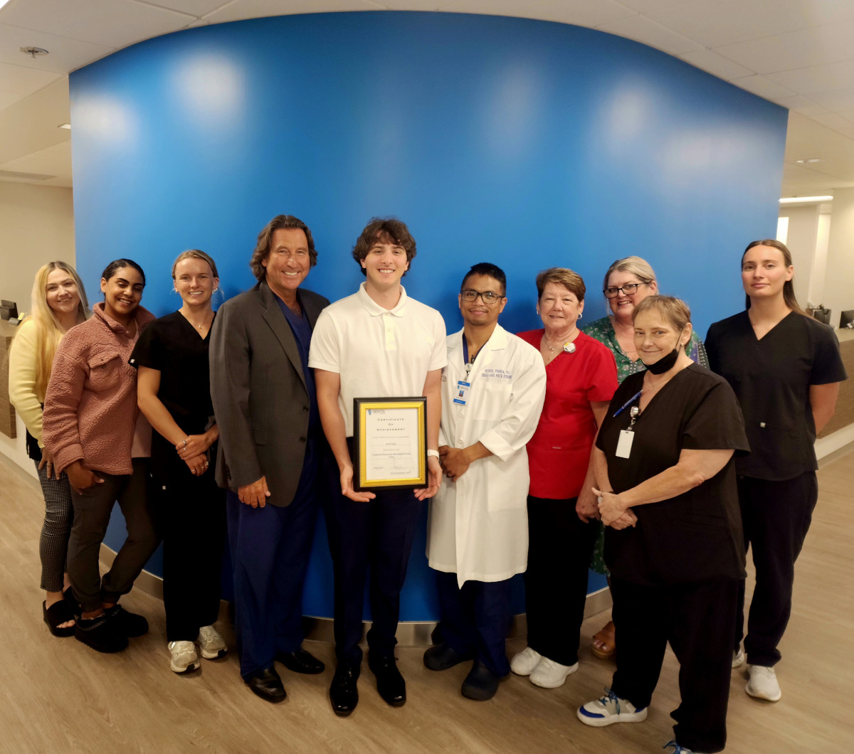 Jacob Lang standing with Dr. Mansfield and his team while holding his internship diploma